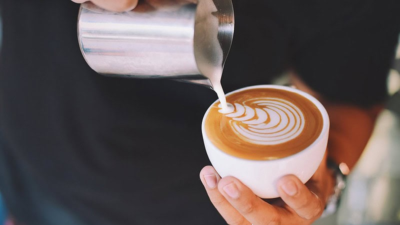 Man sieht eine Hand die gerade Milch in einen Kaffee kippt ein Bild erschafft- Barista Basic Schulung in Dresden