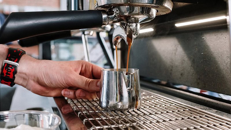 man sieht eine Siebträgermaschine, die einen Behälter mit Kaffee befüllt- Barista Basic Schulung in Dresden