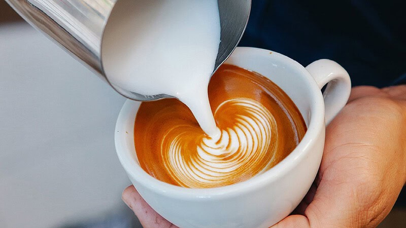 Man sieht wie jemand eine Tasse Kaffee mit Milch befüllt- Barista Kurs mit eigener Maschine und Mühle