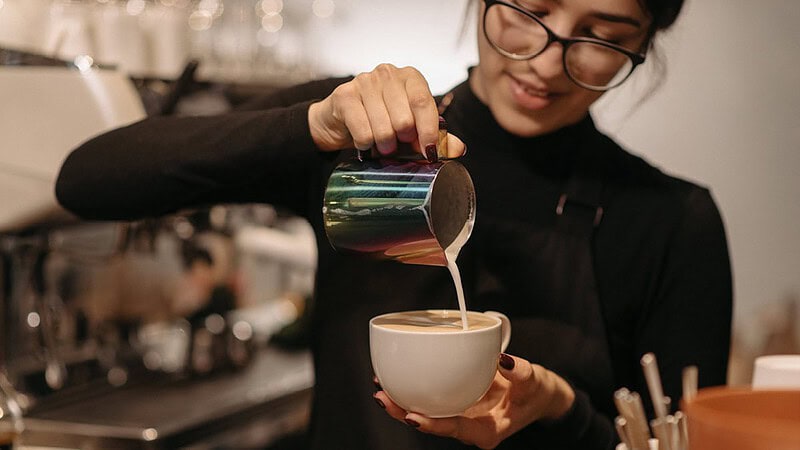 Man sieht eine Frau, die Milch in eine Tasse Kaffee kippt- Barista Professional Schulung in Dresden