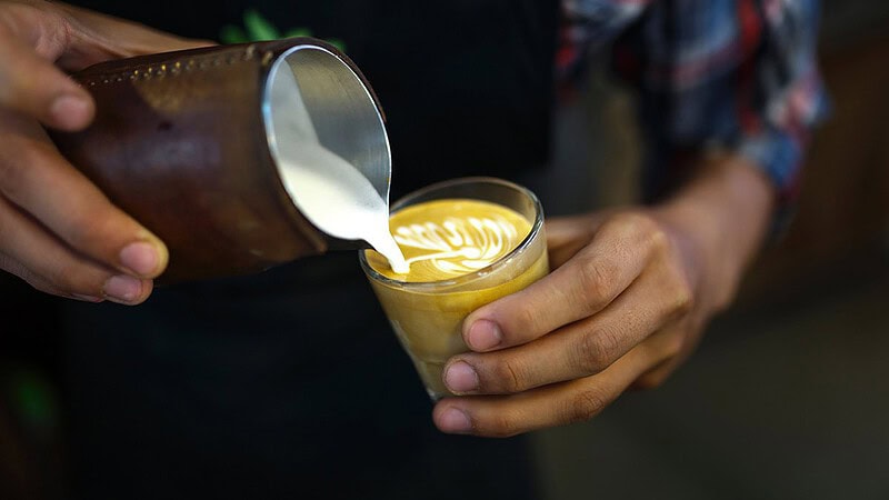 Man sieht jemanden der Milch in eine Tasse Kaffee kippt- Barista Professional Schulung in Dresden