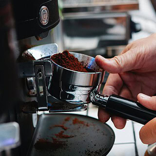 Man sieht eine elektrische Kaffeemühle, die einen Siebträger mit Kaffeepulver füllt- Barista Professional Schulung in Dresden