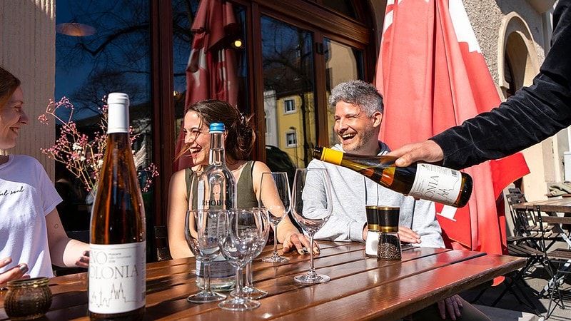 Menschen lachen beim einer Weinverkostung draußen vor dem JuBo Restaurant