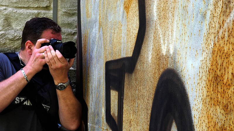 Ein Mann fotografiert mit seiner Kamera eine mit Graffiti bemalte Wand. - Fotokurs Tagesworkshop