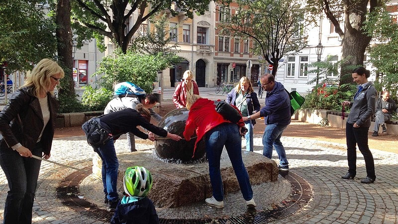 Gruppe sucht nach einem Geocach an einem Brunnen beim Geocaching Schatzrundgang