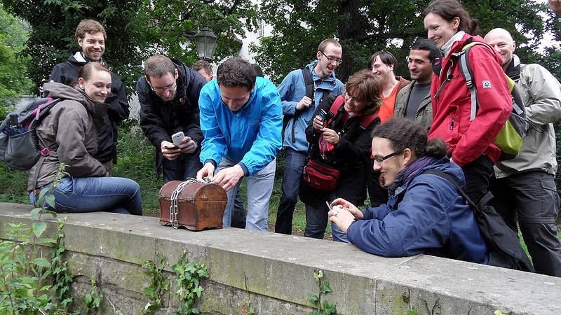 Gruppe von Menschen öffnet einen Geocach in einer Schatztruhe bei der Team Challenge