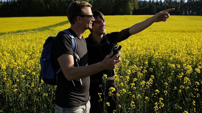 Zwei Männer suchen Geocach mit Kompass im Feld bei der Team Challenge Schnitzeljagd