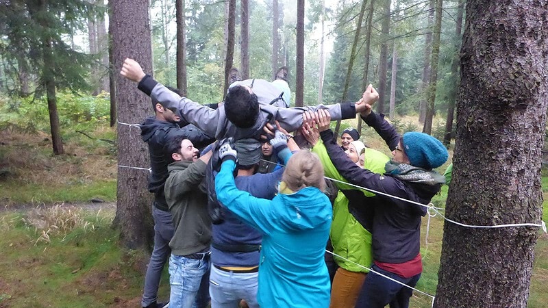 Gruppe hebt eine Person über ein Hindernis bei der Team Challenge Schnitzeljagd