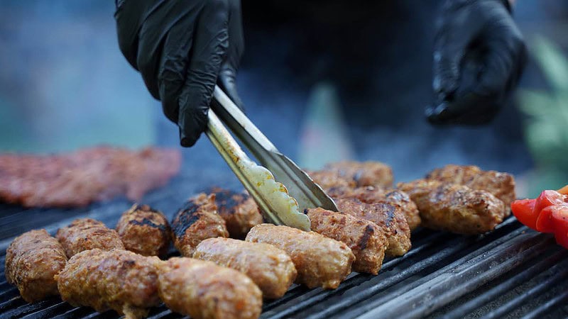 Eine Person grillt Fleisch und Gemüse auf einem Grill