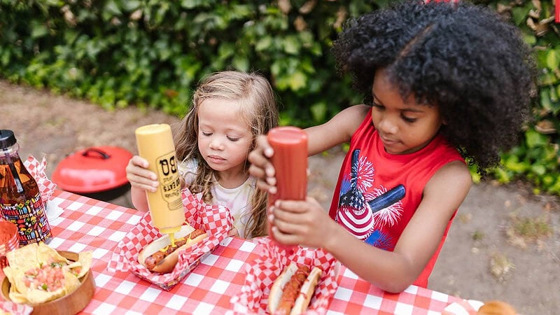 Zwei kleine Mädels essen Hotdogs mit Ketchup und Senf