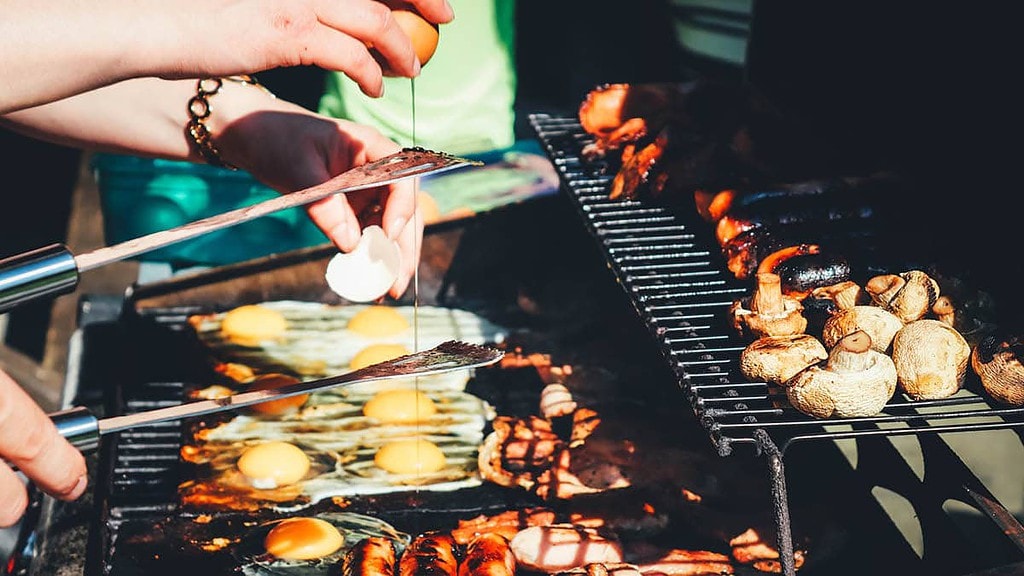 Personen grillen Eier und Champignons auf einem Grill