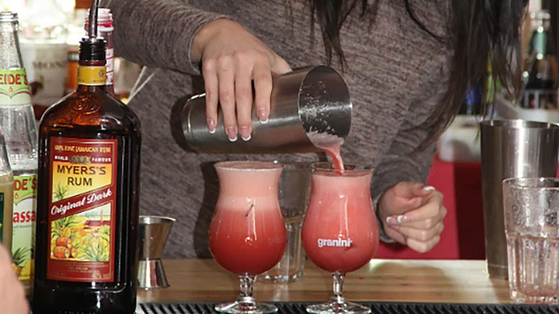 Frau gießt Cocktail aus dem Shaker ins Glas beim Cocktail Aufbaukurs in Dresden