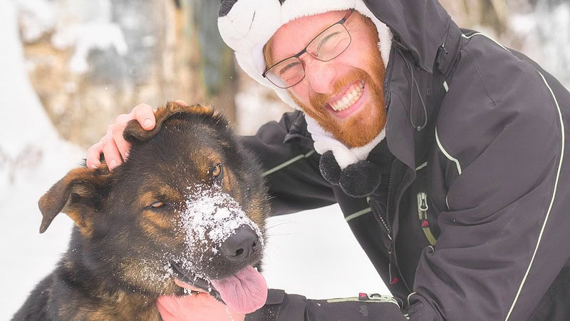 Mann lächelt in die Kamera, Hund nebenan