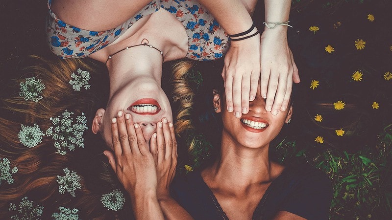 2 Frauen halten sich gegenseitig die Augen zu und lachen