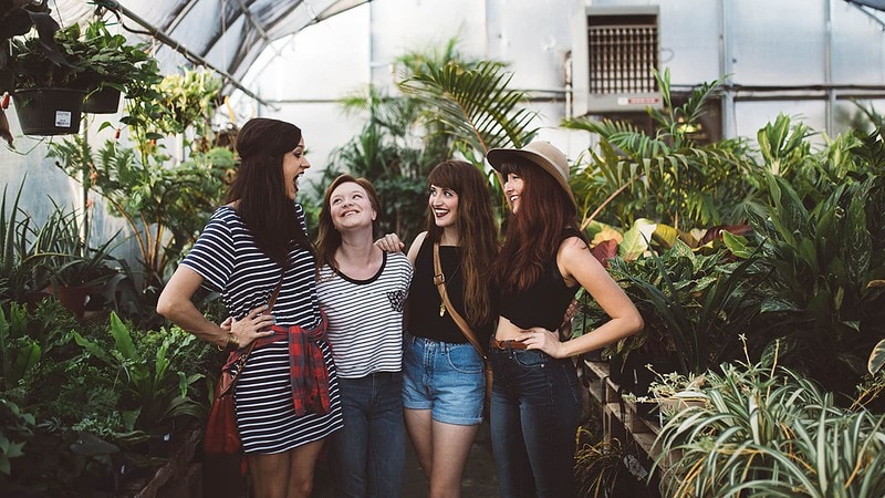 4 Frauen in einem Gewächshaus, alle lachen, im Hintergrund stehen Palmen