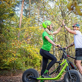 Mann und Frau klatschen ein und stehen auf einem Monterroller und Fahrrad