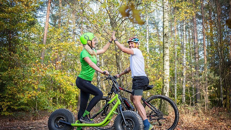 Mann und Frau klatschen ein und stehen auf einem Monterroller und Fahrrad