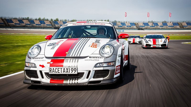 Porsche 911 GT3 fährt auf einer Rennstrecke im Hintergrund weitere Rennwagen sind zu sehen. Der Himmel ist blau.