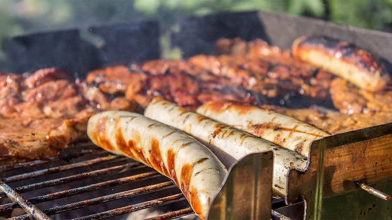 Mehrere Steaks und Bratwürstchen brutzeln auf einem Grill.