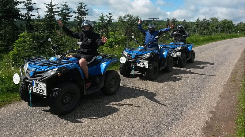 Drei Quadfahrer freuen sich mit in die Luft gestreckten Armen auf den Quads.