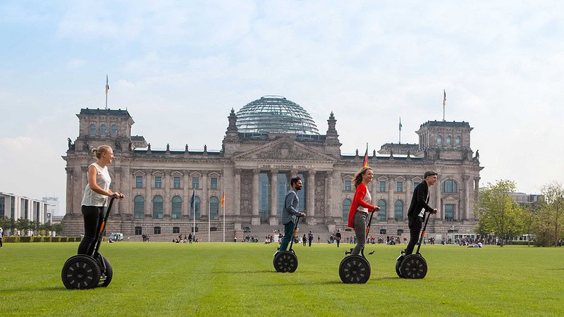 vier Menschen fahren mit Segways vor dem Deutschen Bundestag in Berlin