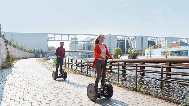 zwei Menschen fahren Segway auf einem Fußweg