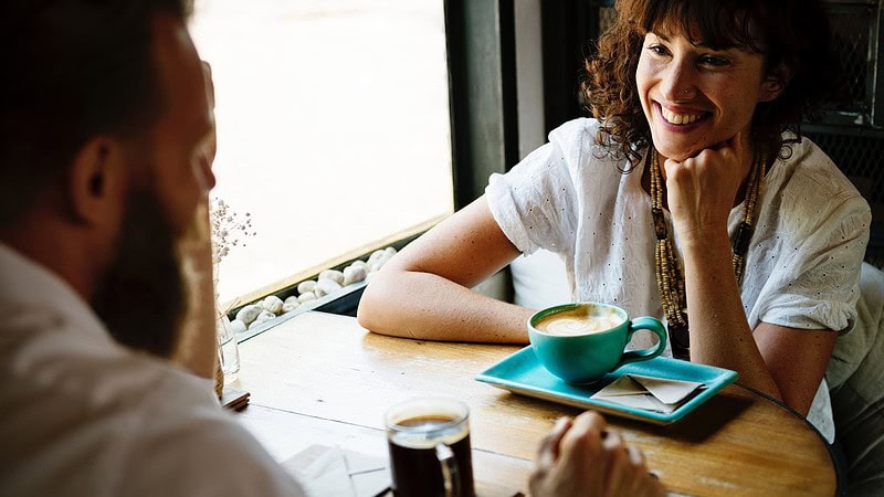 Mann und Frau sitzen am Tisch und trinken Kaffee und lachen zum Speeddating in Sachsen