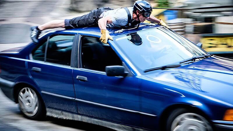 Stuntman fährt auf dem Dach eines Autos und trägt einen Helm