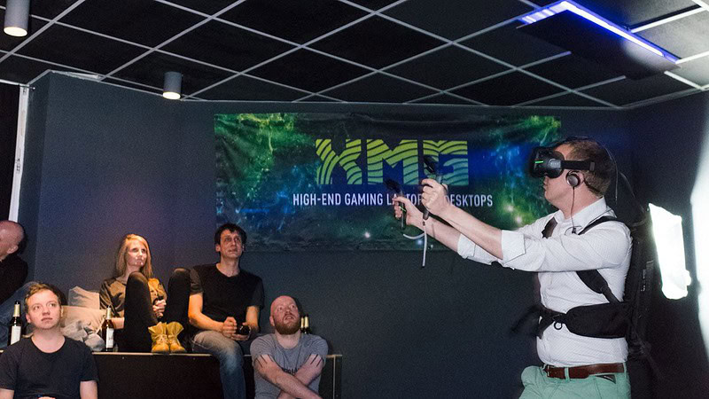 Mann spielt VR Spiel, zwei andere schauen zu