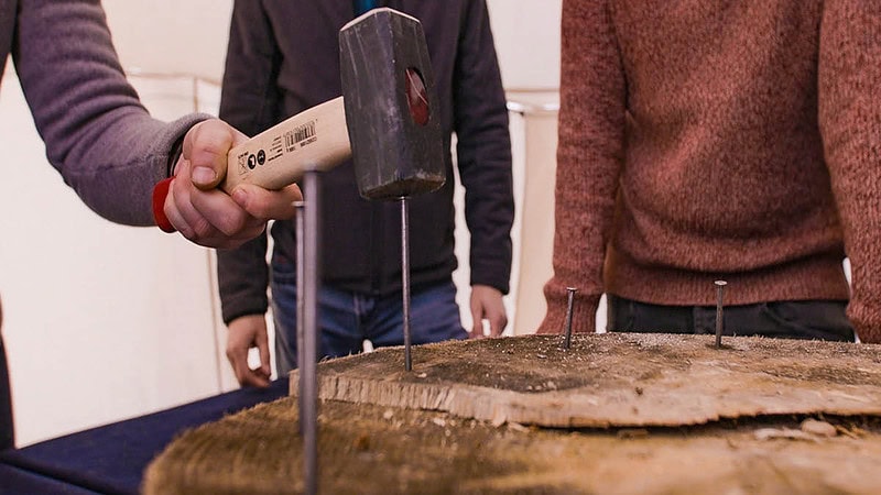 Ein Mann schlägt einen Nagel in ein Holzbrett.