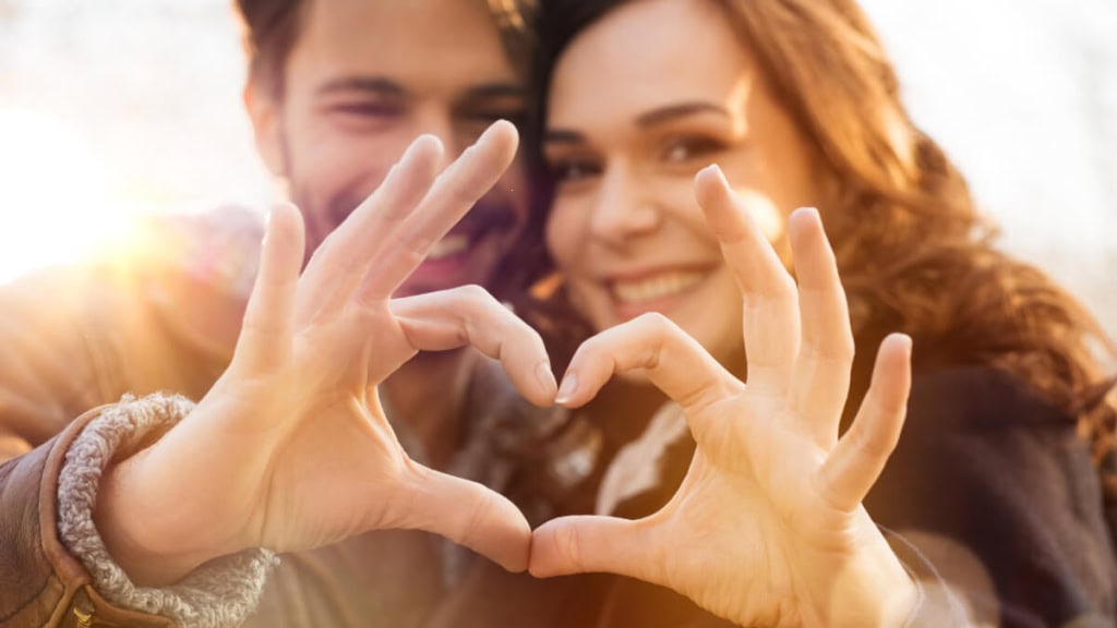 Das Paar posiert zusammen für ein Foto, wobei sie ihre Finger in Form eines Herzens aneinanderlegen