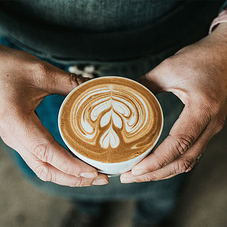 Eine Person hält eine Tasse frisch gebrühten Kaffee in den Händen.