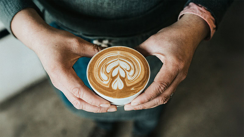 Eine Person hält eine Tasse frisch gebrühten Kaffee in den Händen.