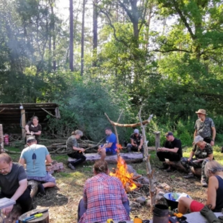 12 Menschen sitzen um ein Lagerfeuer herum