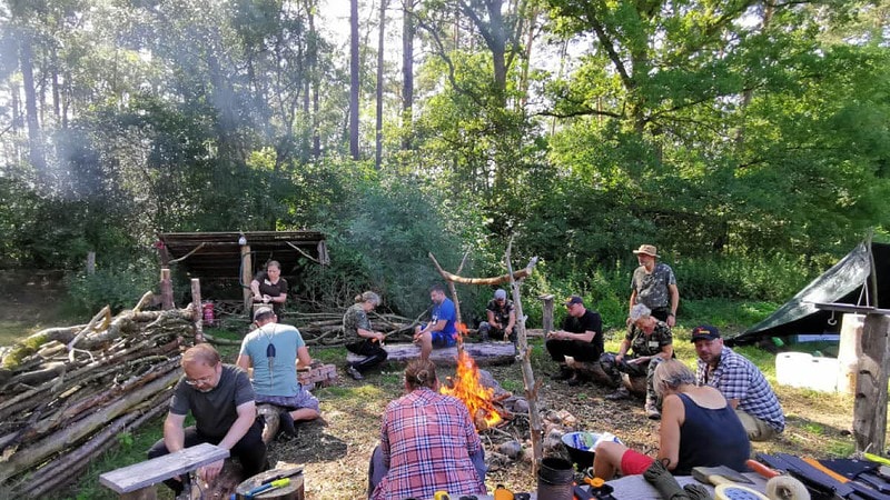 12 Menschen sitzen um ein Lagerfeuer herum