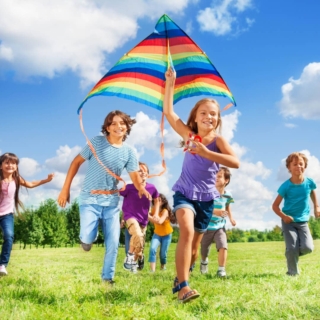 eine Gruppe von Kindern rennt auf einer Wiese und lässt Drachen steigen