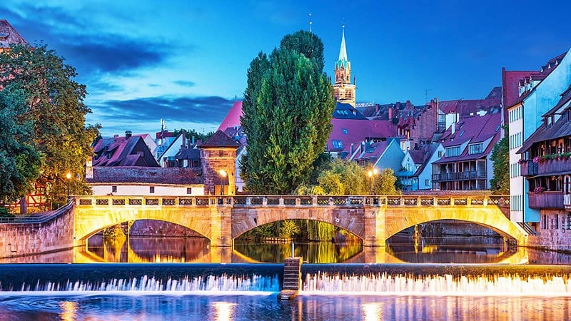 Blick auf die bunte Stadt Nürnberg, beleuchtete Brücke im Vordergrund