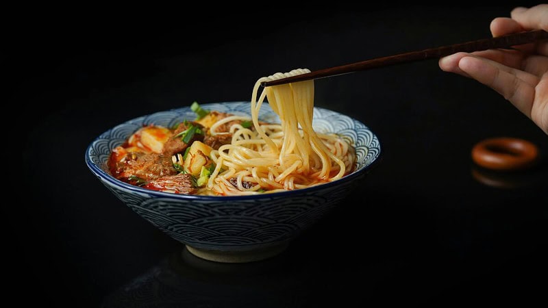 Ramen-Gericht in einer Schüssel, eine Personen hält Stäbchen in der Hand