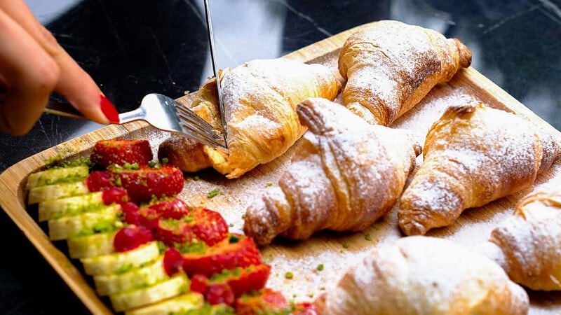 eine Frau schneidet Croissants, serviert auf einem Obstbrett