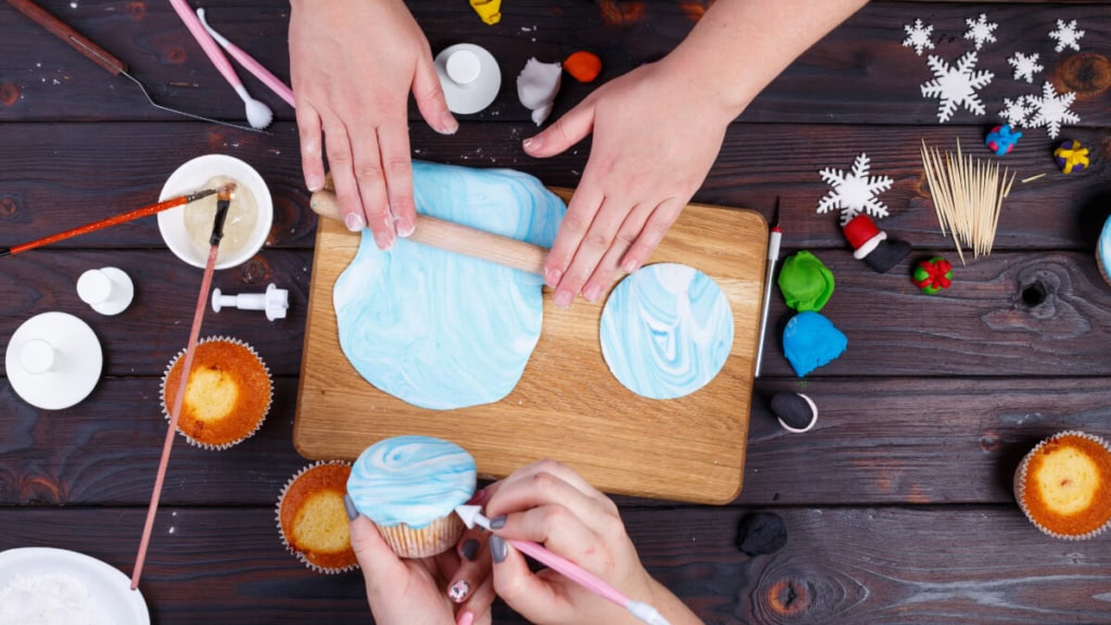 Zwei Frauen dekorieren weihnachtlichen Cupcakes mit Rollfondant