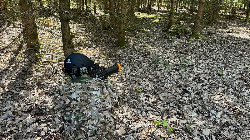 Ein durch die Tarnkleidung schwer erkennbarer Lasertag Spieler, der auf dem Waldboden zwischen Laub liegt.