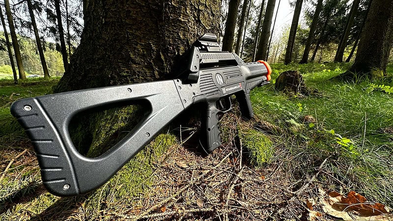 Ein Lasertag Gewehr welches in einem Wald an einen Baum lehnt.