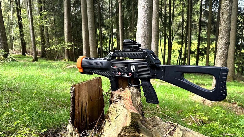 Schwarzes Lasertag Gewehr, welches auf einem Baumstupf in einem Wald Steht.