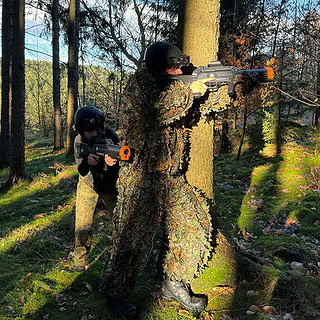 Lasertag Spieler mit Tarnkleidung die sich hinter einem Baum verstecken und in den Wald zielen.