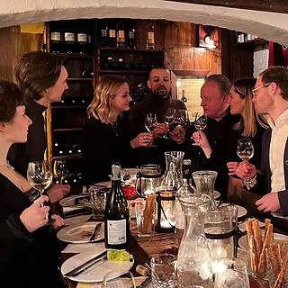 Eine Gruppe schick angezogener Leute, stößt in einem gemütlichen Wein Lokal an.