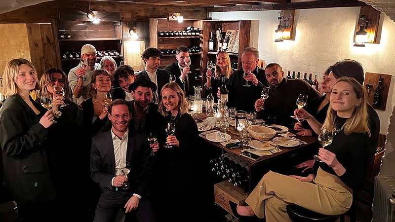 Große Gruppe an Leuten die in die Kamera Lächeln und ihren wein zeigen. Sie Befinden sich in einem gemütlichem wein Lokal.