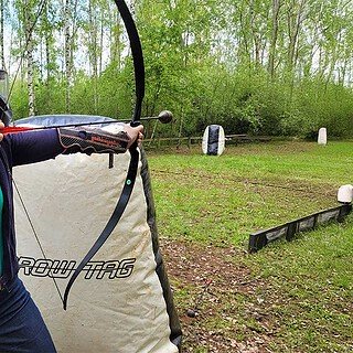 Eine Frau steht hinter einem Hindernis und zielt mit einem Boge beim Arrowtag bei Leipzig.