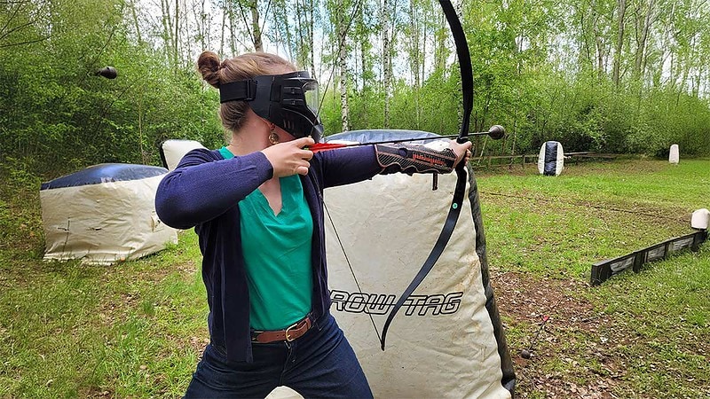 Eine Frau steht hinter einem Hindernis und zielt mit einem Boge beim Arrowtag bei Leipzig.