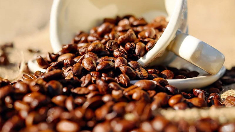 Aus einer umgekippten Tasse sind Kaffeebohnen verteilt.