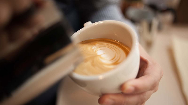 In eine Kaffeetasse wird Milch aufgegossen.